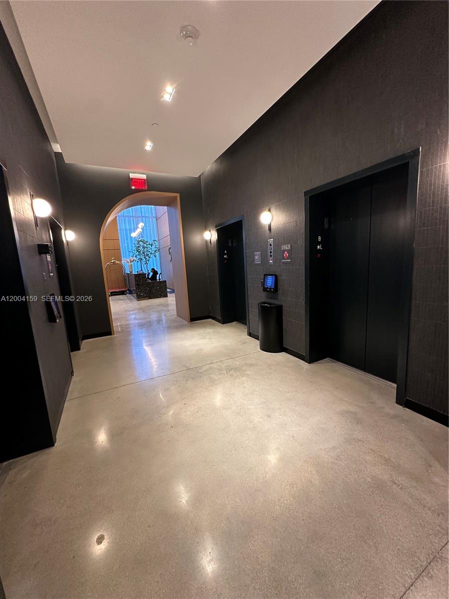 A modern elevator lobby features dark textured walls, polished concrete floors, and a recessed archway — 121 NE 5 # 2712, Miami FL 33132, MIAMI, FL