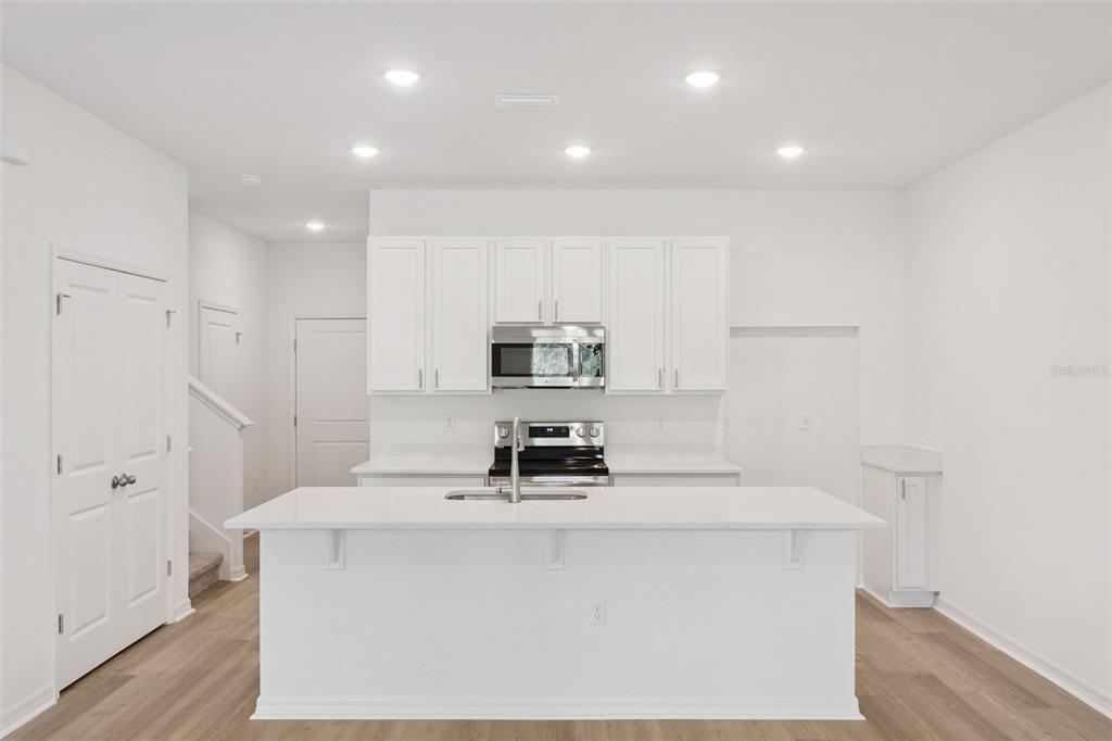 A modern kitchen features white cabinetry, a large central island, and stainless steel appliances — 2294 RED PINE COURT, EUSTIS, FL