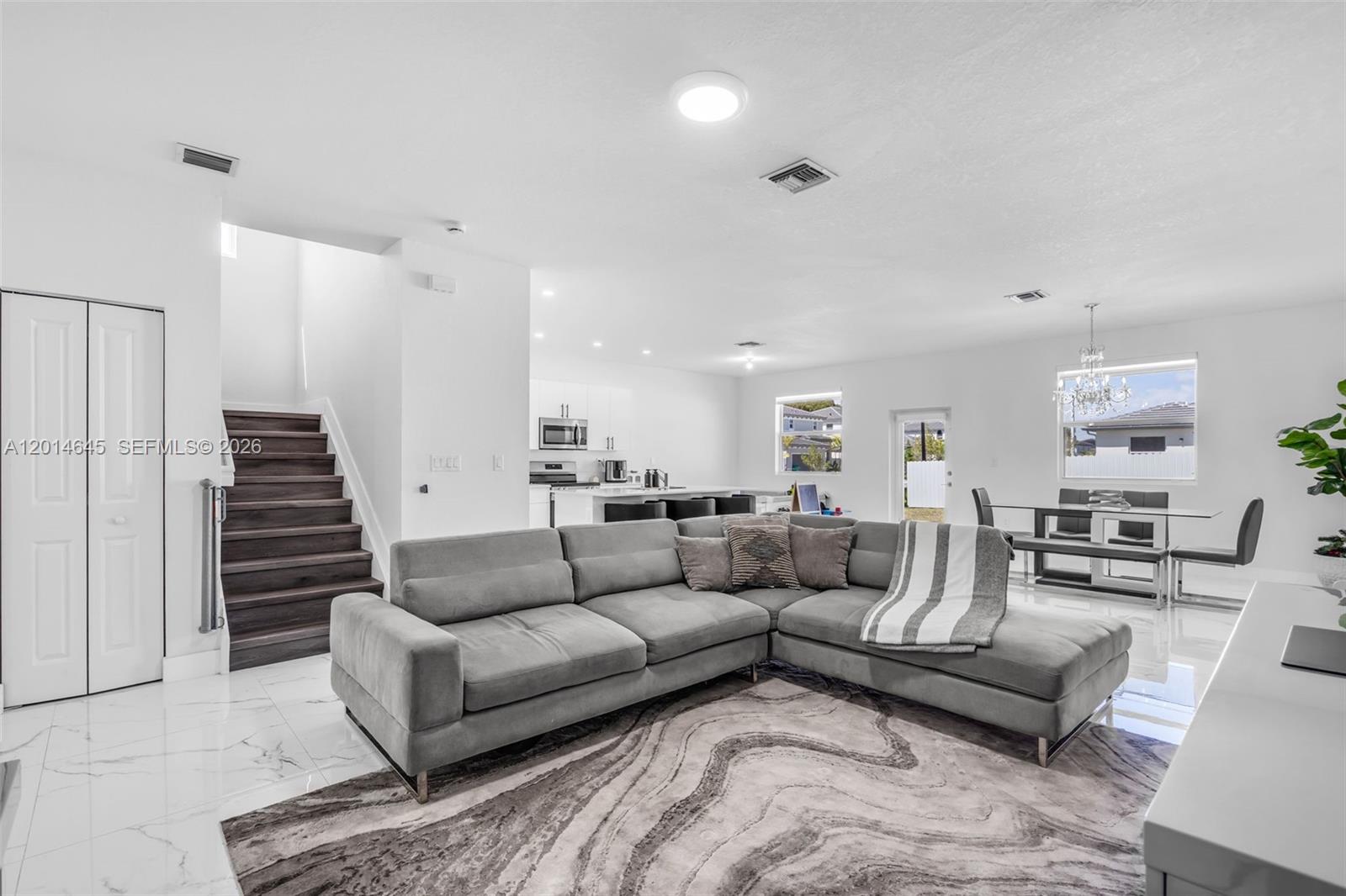 A modern open-concept living room features a gray sectional sofa, white tile floors, and stairs — 13629 SW 186th Ln, Miami FL 33177, MIAMI, FL