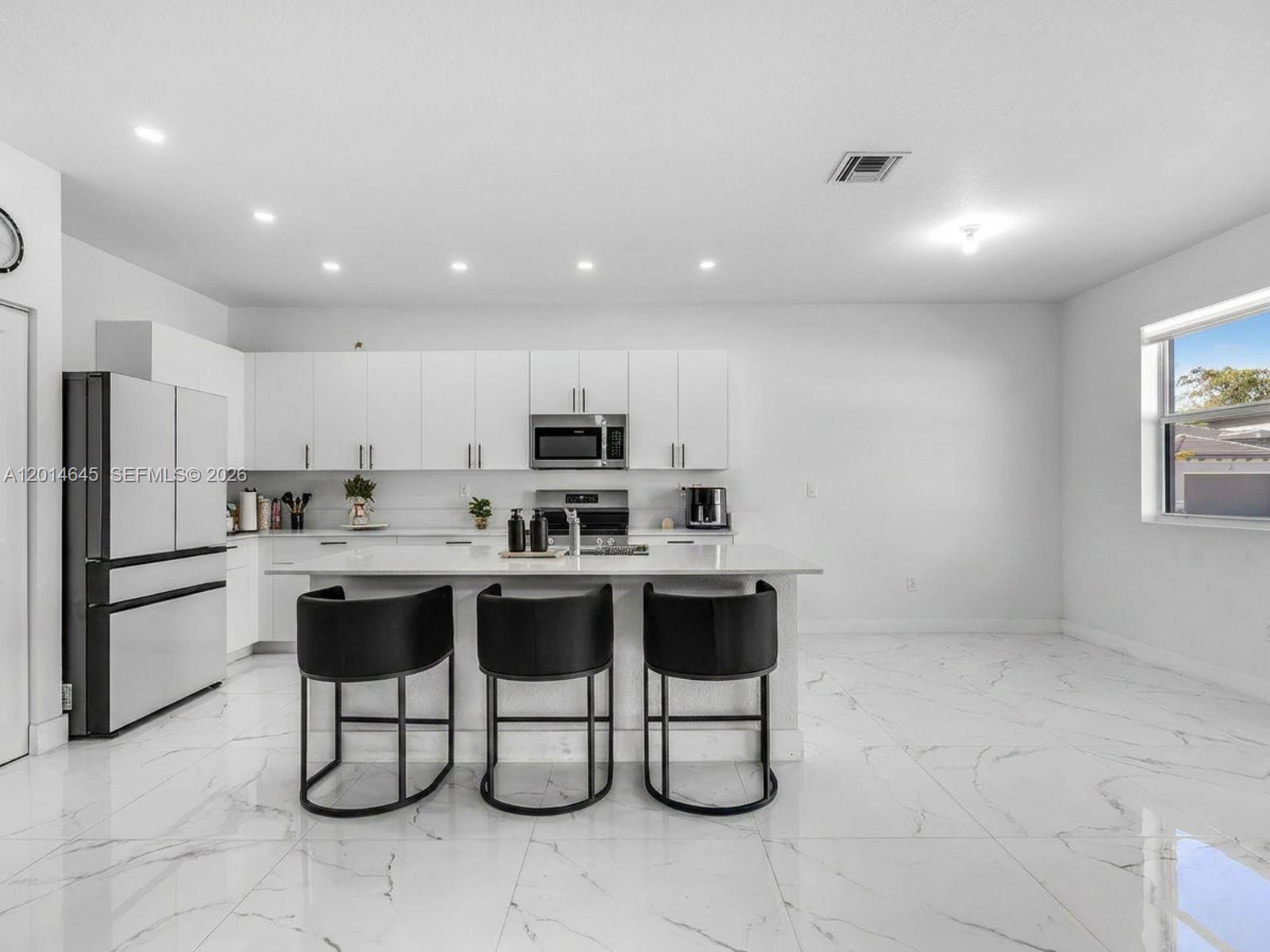 A modern kitchen features white cabinets, a central island with three stools, and marble flooring — 13629 SW 186th Ln, Miami FL 33177, MIAMI, FL