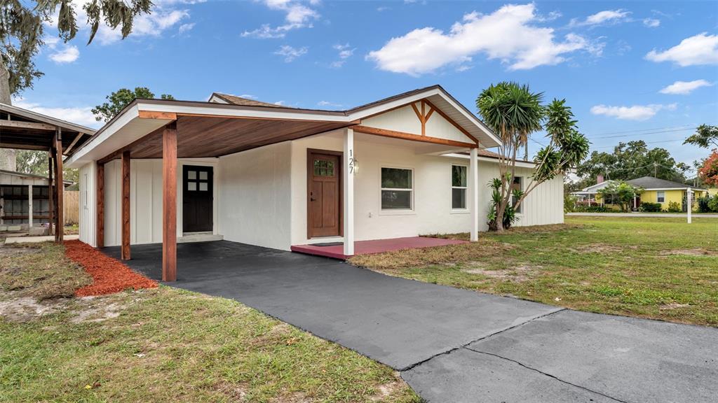 A white house with a wooden-ceiling carport, a brown front door, and a paved driveway — 127 COLONIAL DRIVE, AUBURNDALE, FL