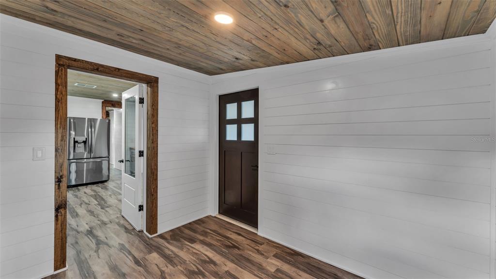 A room with white shiplap walls, a wood-plank ceiling, and a dark wood door — 127 COLONIAL DRIVE, AUBURNDALE, FL