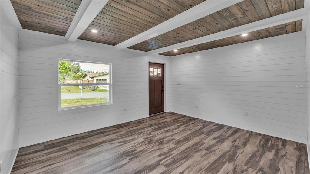 A room with white shiplap walls, a dark wood-paneled ceiling with beams, and wood-look flooring — 127 COLONIAL DRIVE, AUBURNDALE, FL