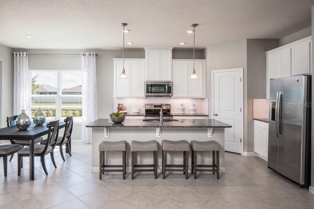 A kitchen features white cabinets, a granite island with four stools, and stainless steel appliances — 2578 WHITE LADYFISH ROAD, WIMAUMA, FL