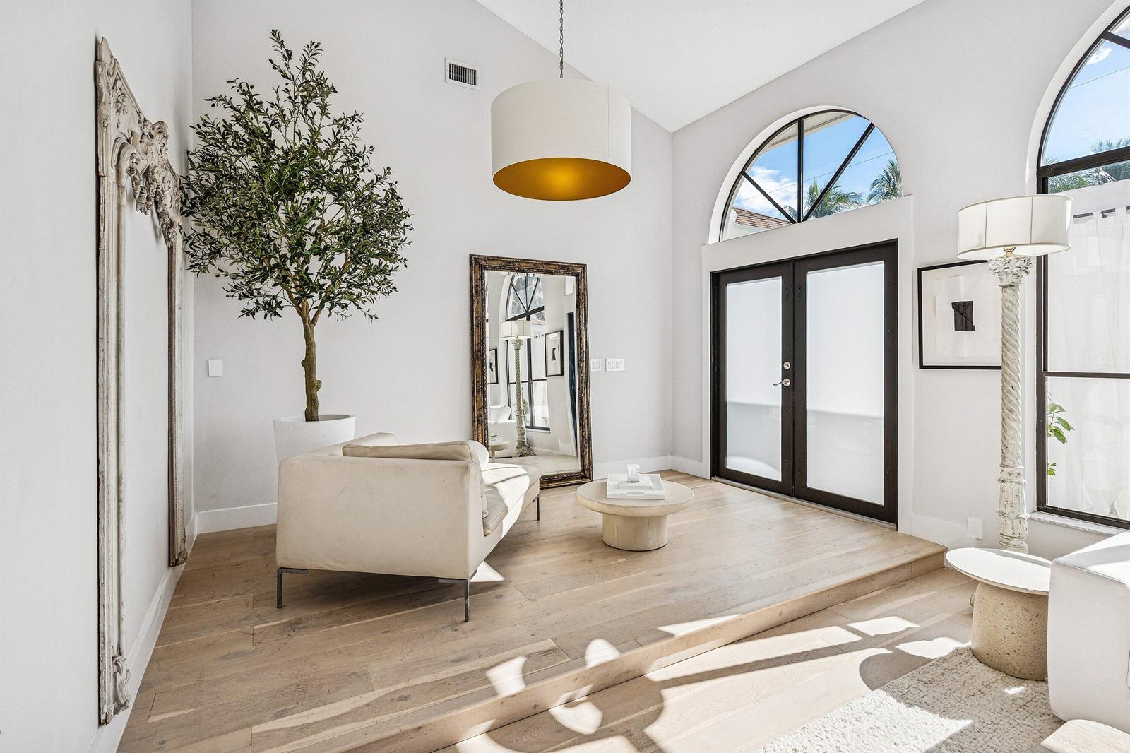 A bright living room features a raised wooden floor, arched windows, and a large mirror — 48 Harbour Drive N, Boynton Beach FL 33435, BOYNTON BEACH, FL