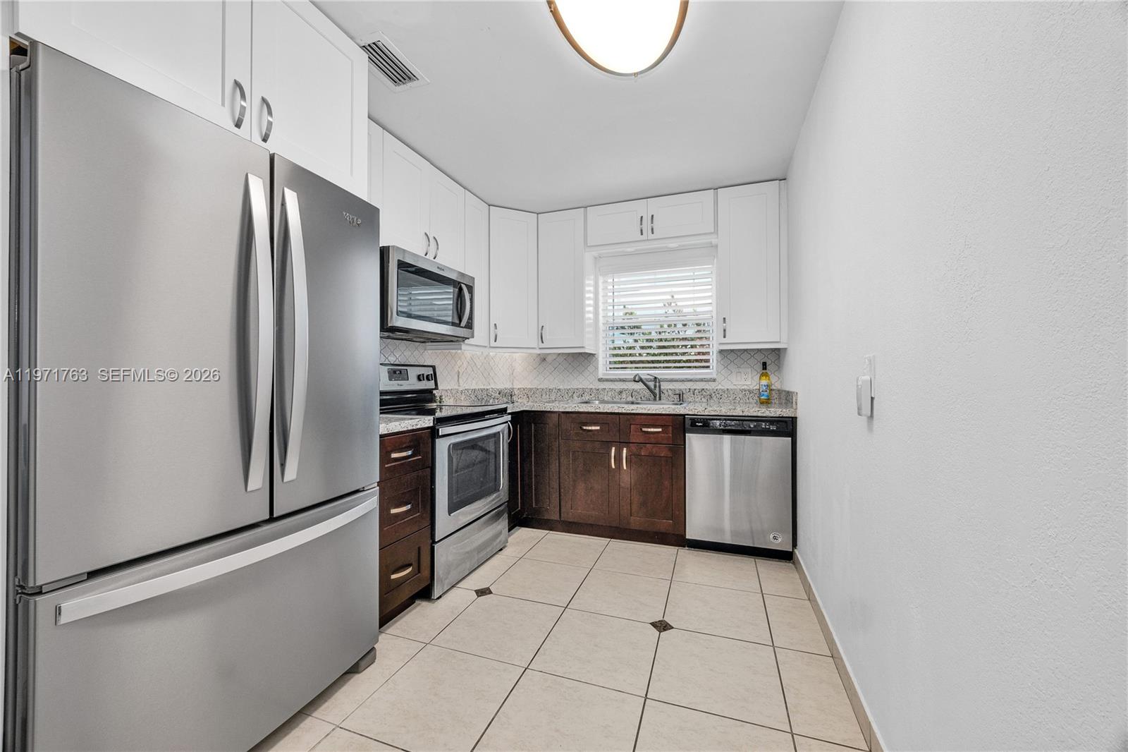 A kitchen features stainless steel appliances, white upper cabinets, dark lower cabinets, and tile flooring — 7785 SW 86th St # 414, Miami FL 33143, MIAMI, FL