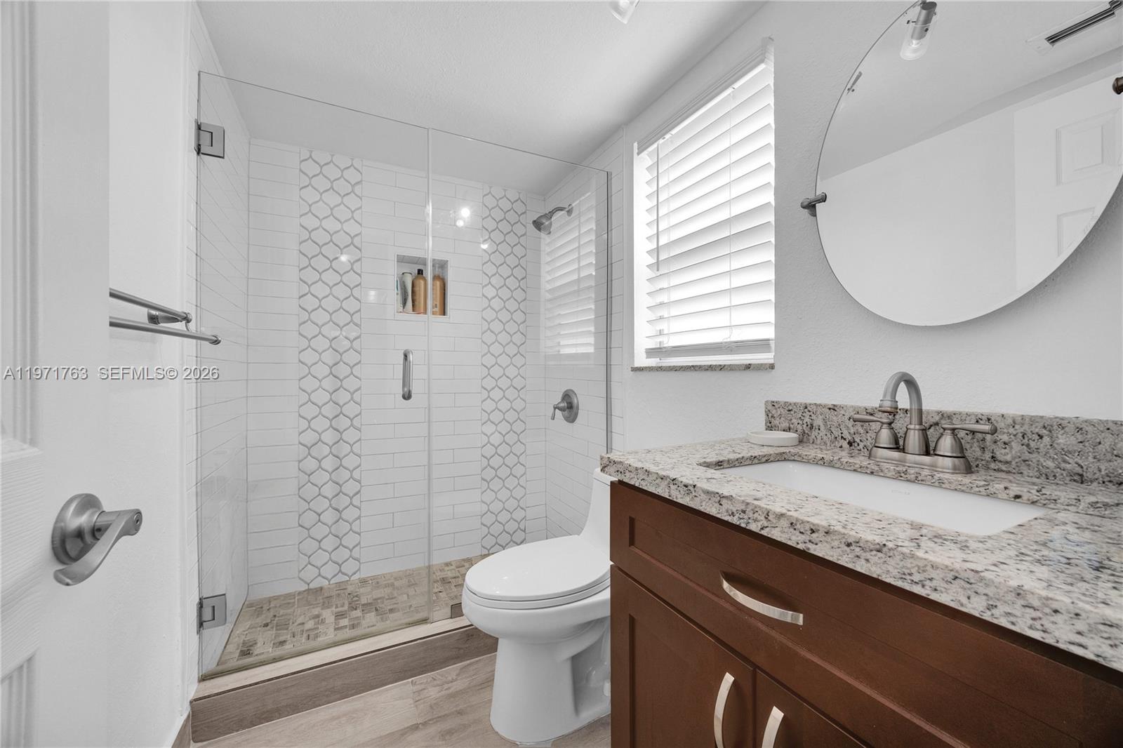 A bathroom features a glass-enclosed shower with patterned tile, a vanity, and a round mirror — 7785 SW 86th St # 414, Miami FL 33143, MIAMI, FL