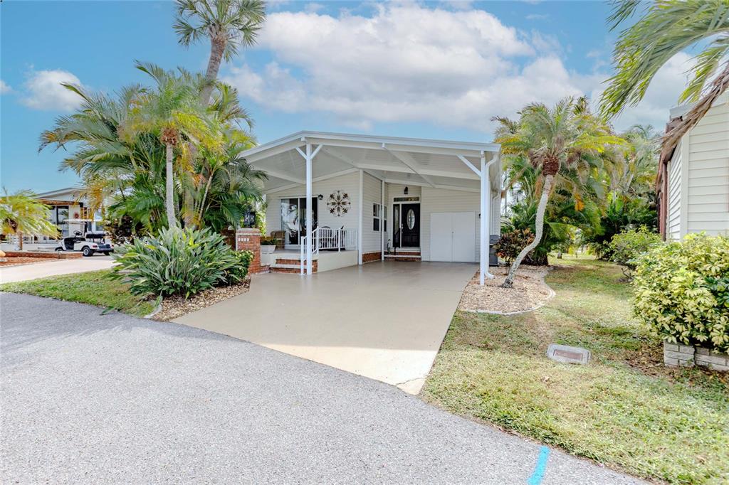A light-colored house features a large covered carport, a front porch, and tropical landscaping — 2100 KINGS HIGHWAY UNIT 1008, PORT CHARLOTTE, FL