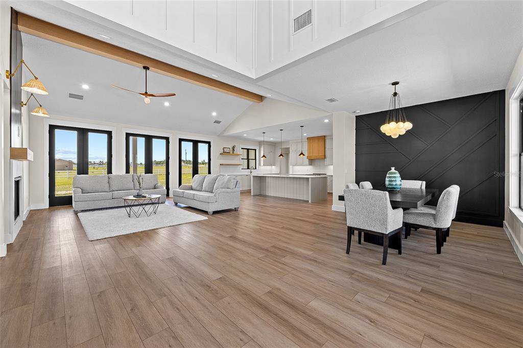 An open-concept living and dining area features vaulted ceilings, wood-look flooring, and a black accent wall — 389 SW MOSSY OAK WAY, LAKE CITY, FL