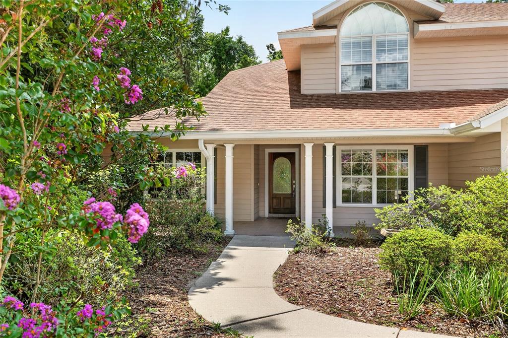 A tan two-story house with a front walkway, white columns, and blooming crape myrtle trees — 5015 NW 71ST PLACE, GAINESVILLE, FL