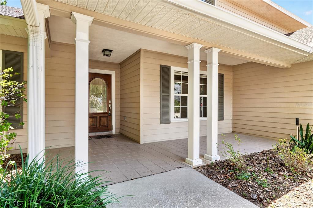 A covered front porch with white columns, a wooden front door, and beige siding — 5015 NW 71ST PLACE, GAINESVILLE, FL