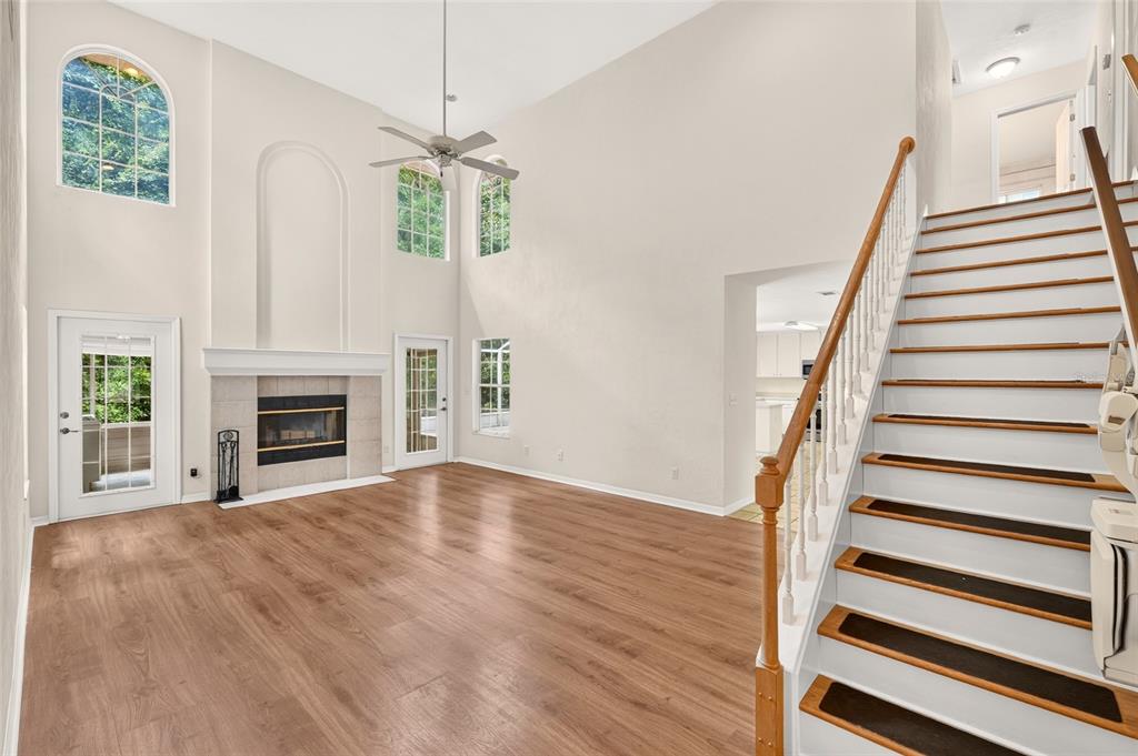 A living room with high ceilings, a fireplace, wood-look flooring, and a staircase — 5015 NW 71ST PLACE, GAINESVILLE, FL