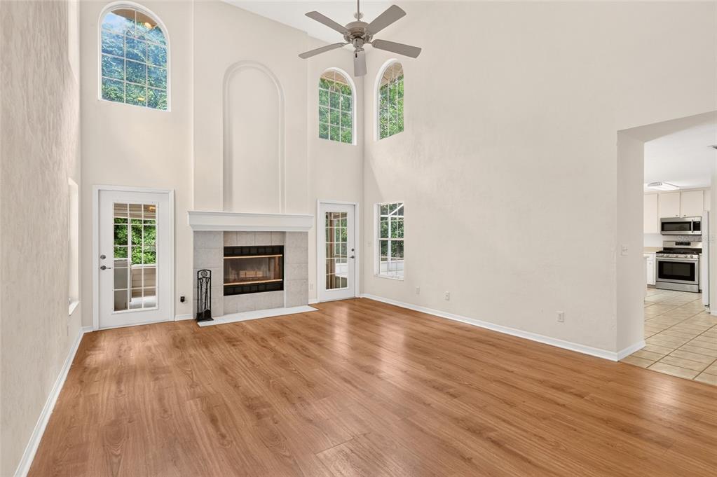 A living room with high ceilings, a fireplace, wood-look flooring, and a ceiling fan — 5015 NW 71ST PLACE, GAINESVILLE, FL