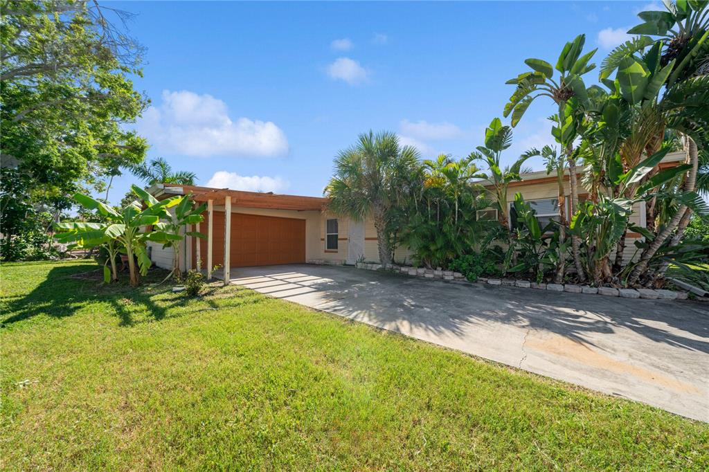A single-story house with a carport, concrete driveway, and lush tropical landscaping under a blue sky — 6903 S SHORE DRIVE S, SOUTH PASADENA, FL