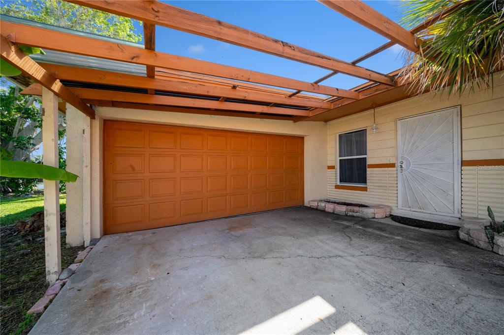 A concrete driveway leads to a garage door under a wooden pergola attached to a house — 6903 S SHORE DRIVE S, SOUTH PASADENA, FL