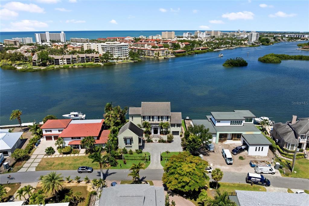 An aerial view shows three waterfront houses along a bay with a distant beach skyline — 6438 HOLLYWOOD BOULEVARD, SARASOTA, FL