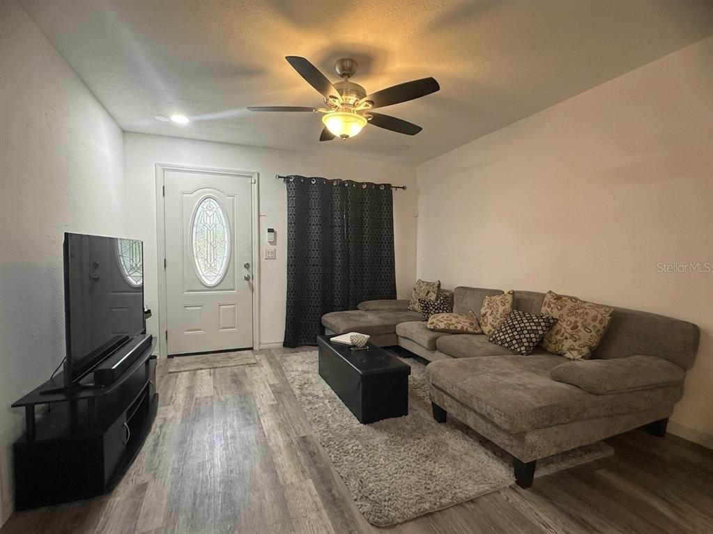 A living room features a sectional sofa, television, ceiling fan, and light wood-look flooring — 636 RAINBOW BOULEVARD, BABSON PARK, FL