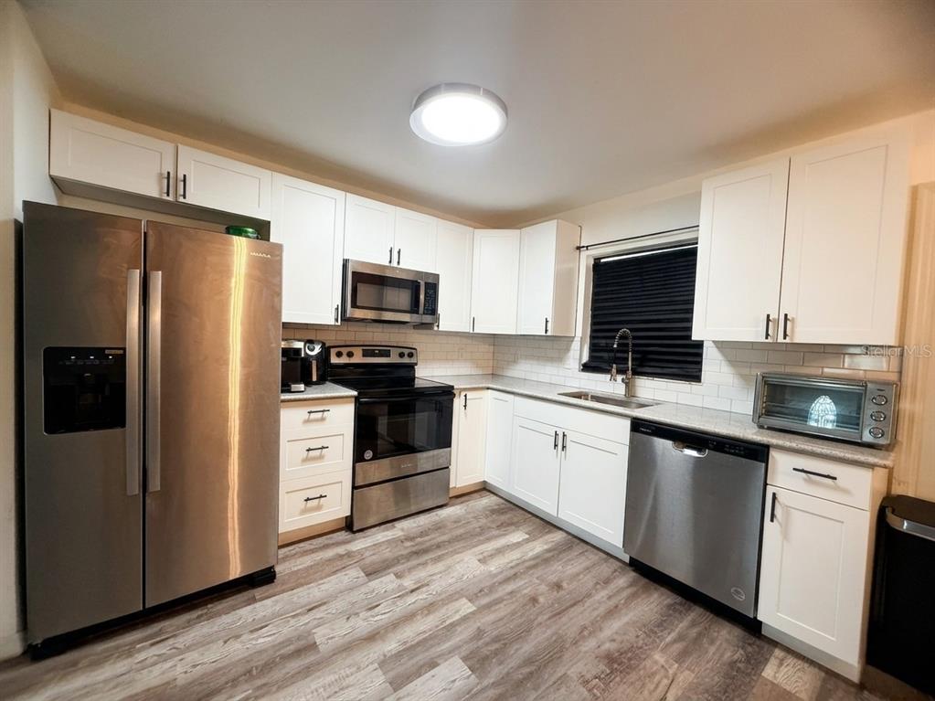 A kitchen features white cabinets, stainless steel appliances, a subway tile backsplash, and wood-look flooring — 636 RAINBOW BOULEVARD, BABSON PARK, FL