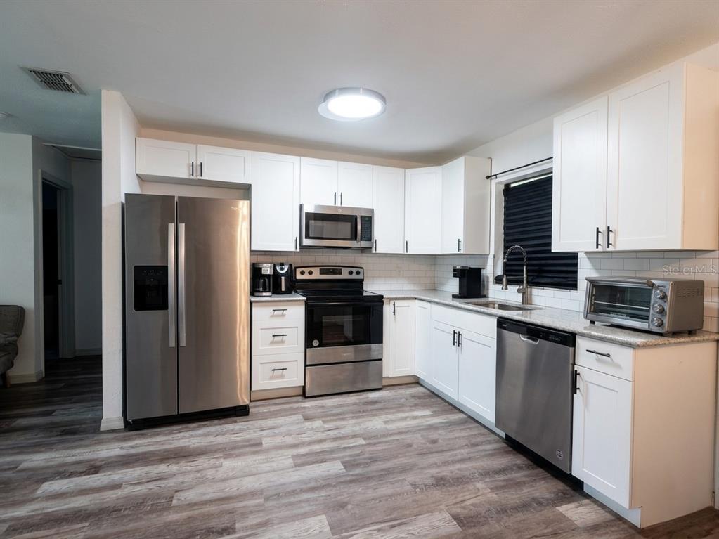A kitchen features white cabinets, stainless steel appliances, and wood-look flooring — 636 RAINBOW BOULEVARD, BABSON PARK, FL