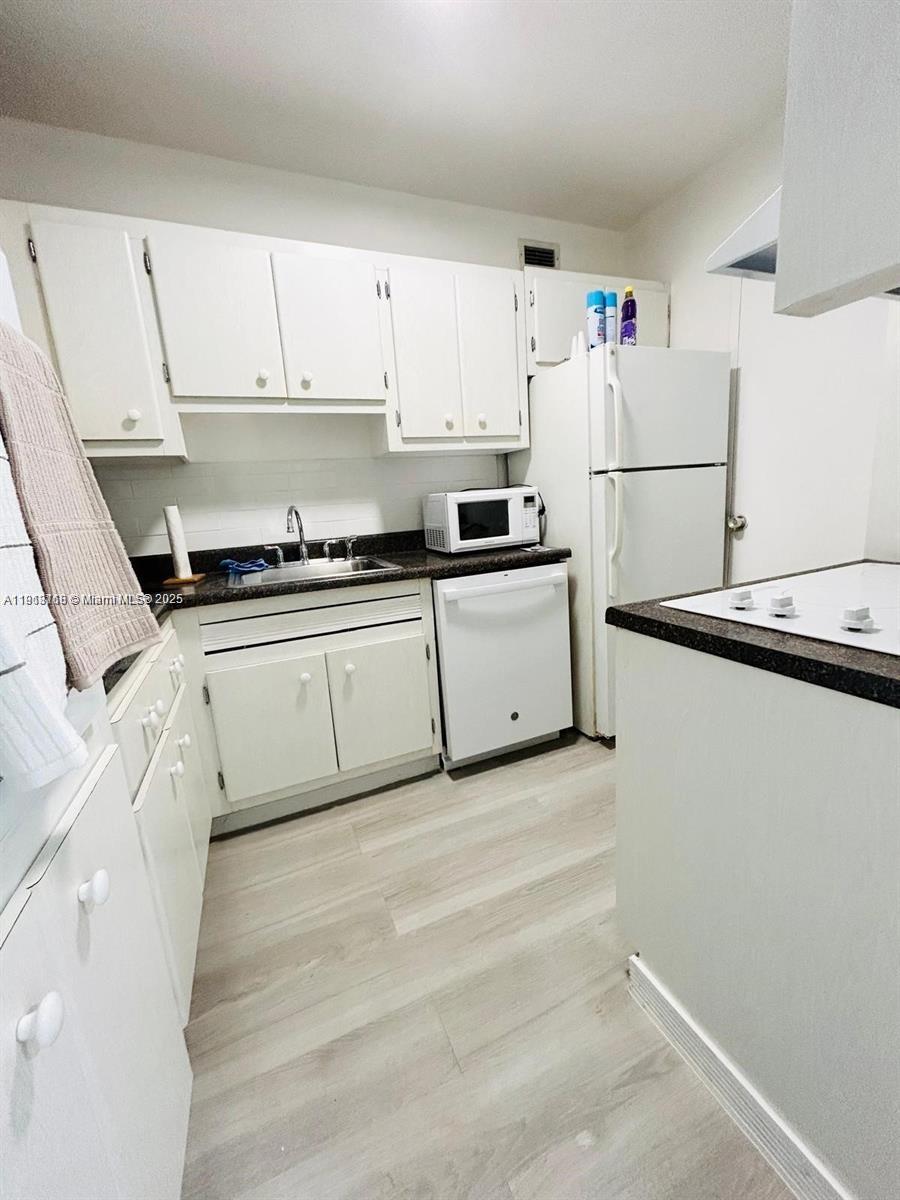 A kitchen features white cabinets, white appliances, a dark countertop, and light wood-look flooring — 100 Lincoln Rd # 535, Miami Beach FL 33139, MIAMI BEACH, FL