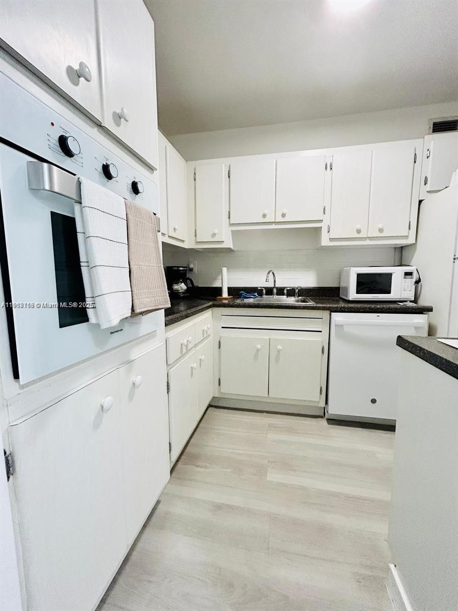 A kitchen features white cabinets, a wall oven, a dishwasher, and light-colored wood-look flooring — 100 Lincoln Rd # 535, Miami Beach FL 33139, MIAMI BEACH, FL