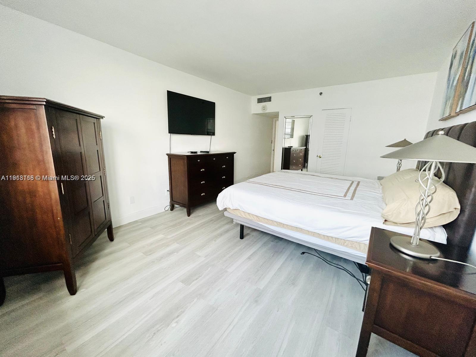 A bedroom features light wood-look flooring, a dark wood armoire, a dresser, and a bed — 100 Lincoln Rd # 535, Miami Beach FL 33139, MIAMI BEACH, FL