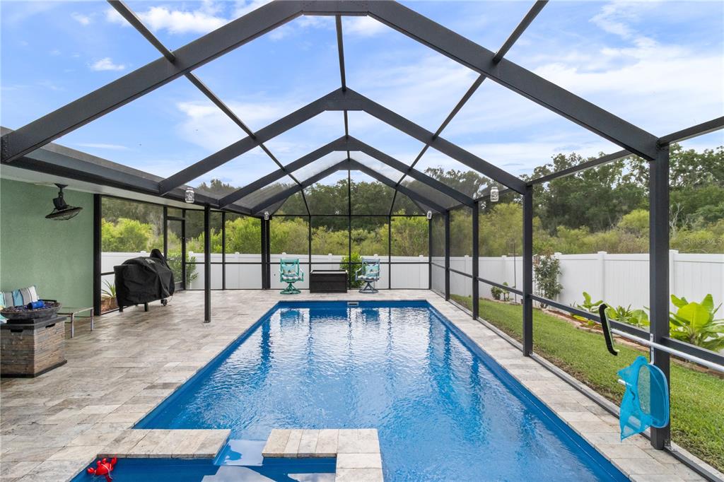 A covered patio features a rectangular swimming pool with a built-in spa and stone pavers — 4562 FAIRWAY OAKS DRIVE, MULBERRY, FL