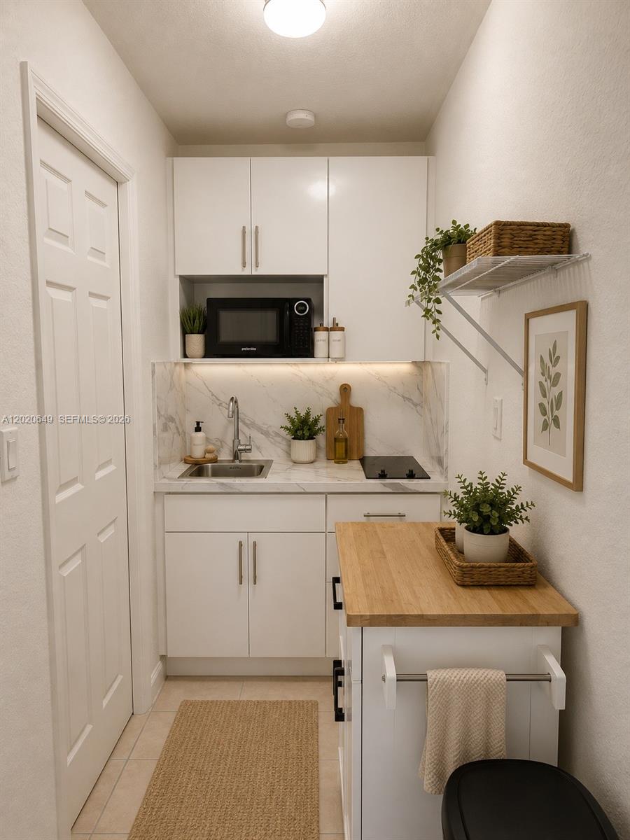 A small kitchenette features white cabinetry, a marble backsplash, a sink, and a wooden island — 12805 SW 116th Ct # 1, Miami FL 33176, MIAMI, FL
