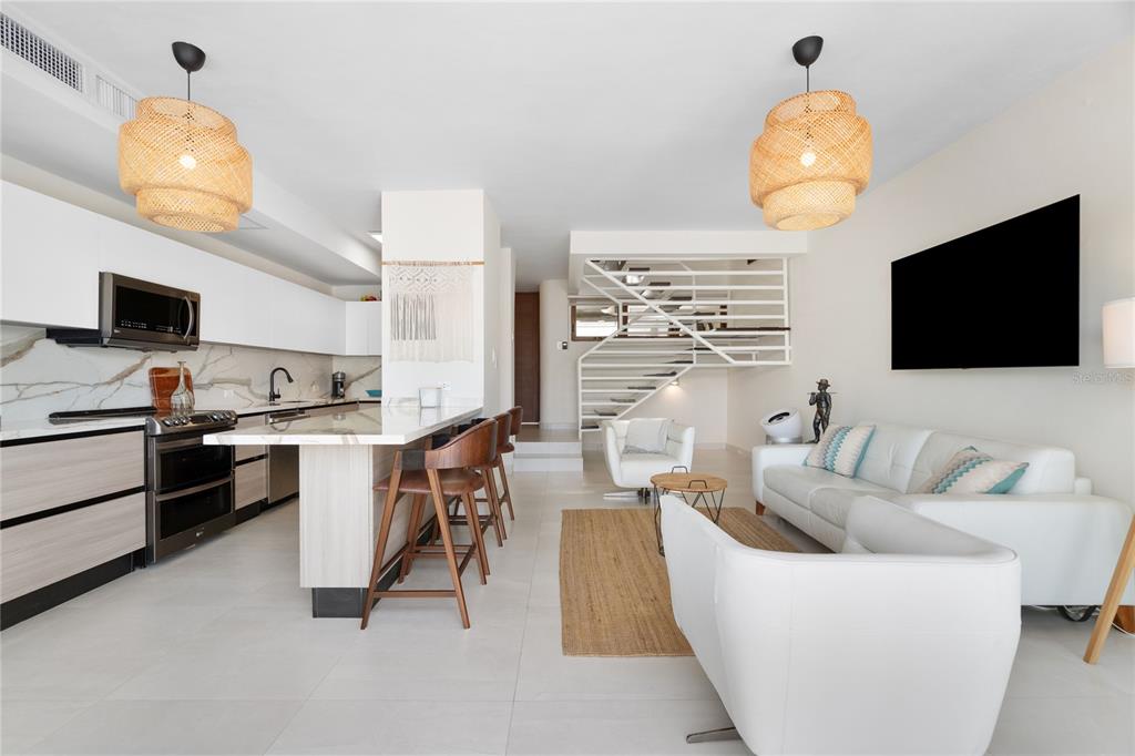 A modern open-concept living room and kitchen featuring white cabinetry, a staircase, and pendant lighting — 260 HARBOUR DRIVE UNIT 13, HUMACAO, PR