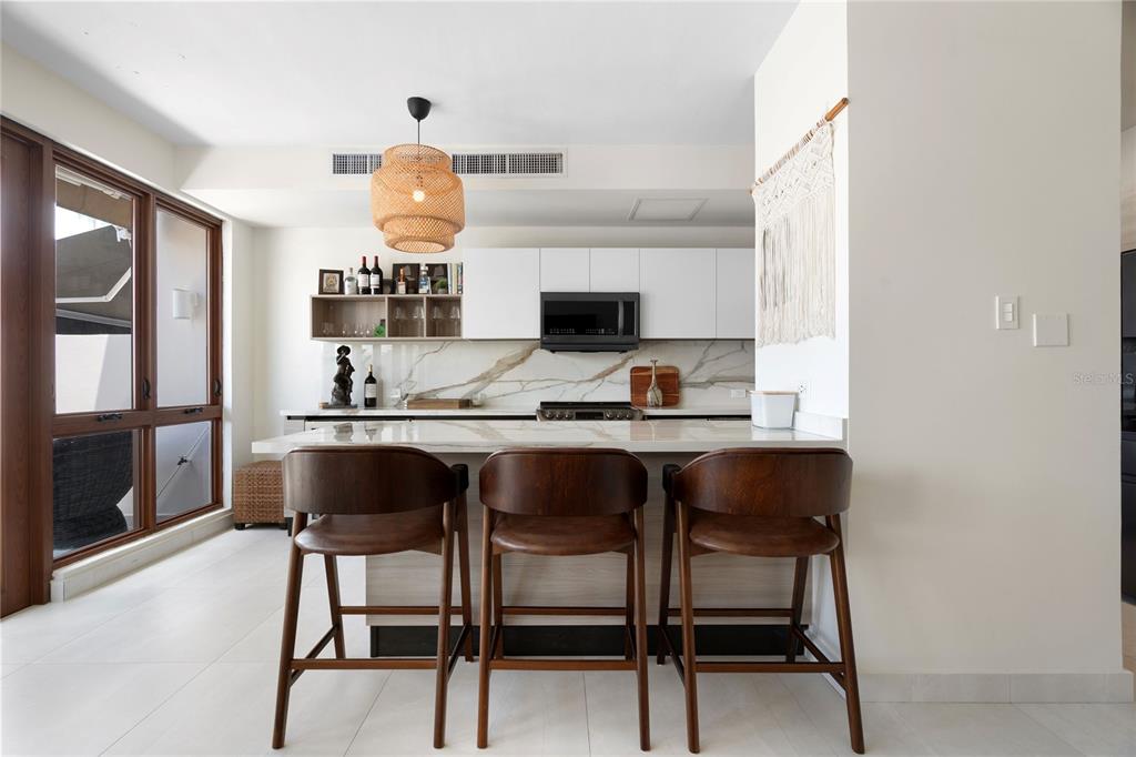 A modern kitchen features white cabinetry, a marble-patterned backsplash, and three wooden bar stools — 260 HARBOUR DRIVE UNIT 13, HUMACAO, PR