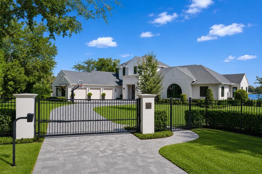 A gated driveway leads to a large white house with a multi-car garage and lawn — 320 EVANSDALE ROAD, LAKE MARY, FL