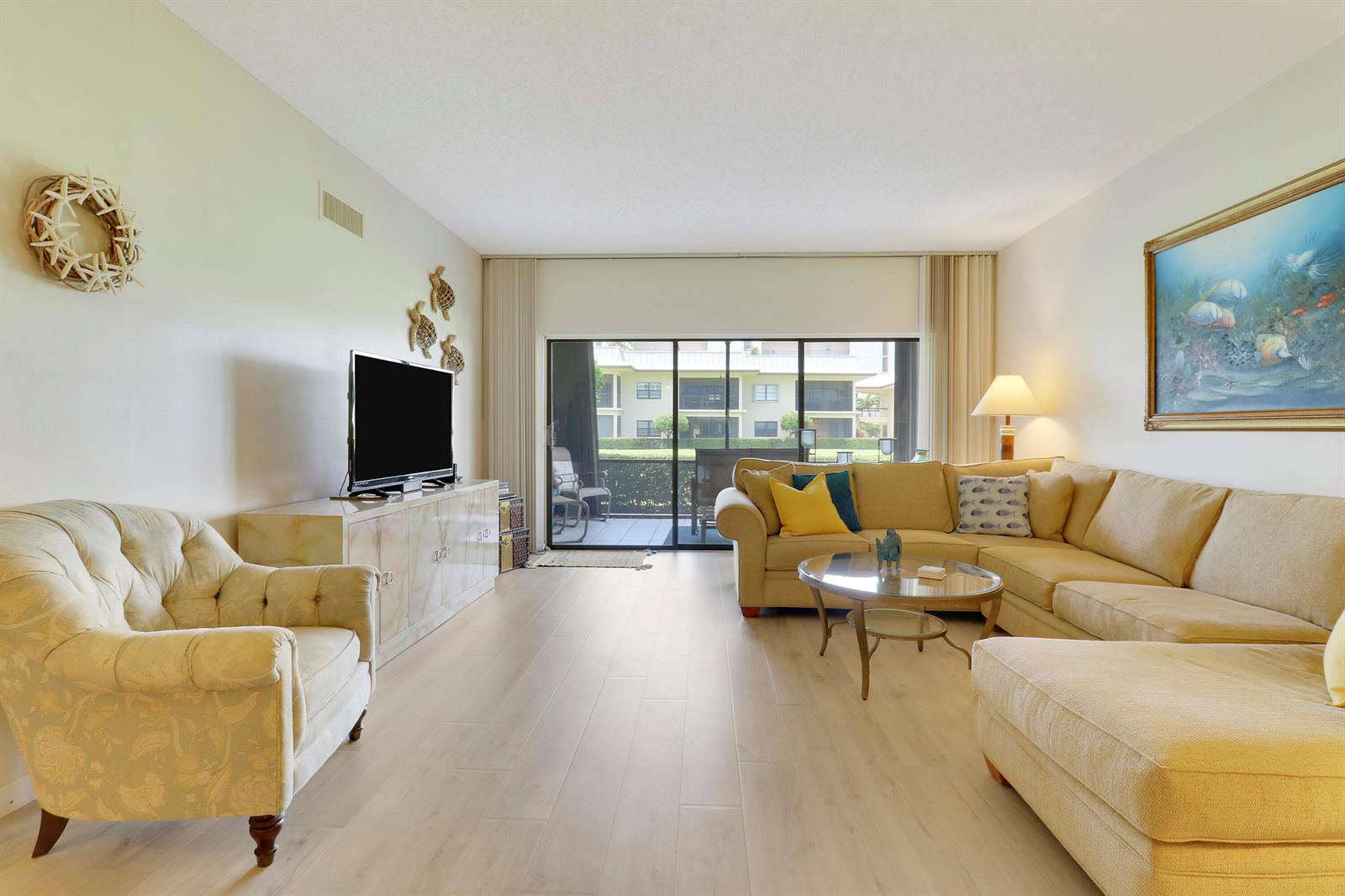 A living room features light wood flooring, a sectional sofa, an armchair, and sliding doors — 275 S Beach Road, Tequesta FL 33469, TEQUESTA, FL