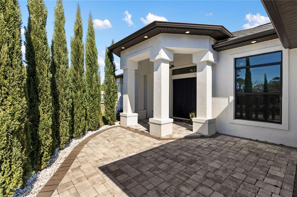 A paved walkway leads to the covered entryway of a white house with tall cypress trees — 2470 ABBOTSFORD STREET, NORTH PORT, FL