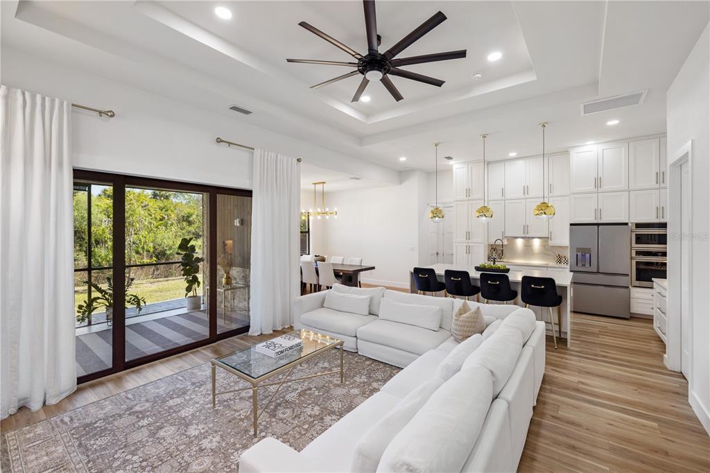 A modern open-concept living room and kitchen featuring white cabinetry, a sectional sofa, and sliding doors — 2470 ABBOTSFORD STREET, NORTH PORT, FL