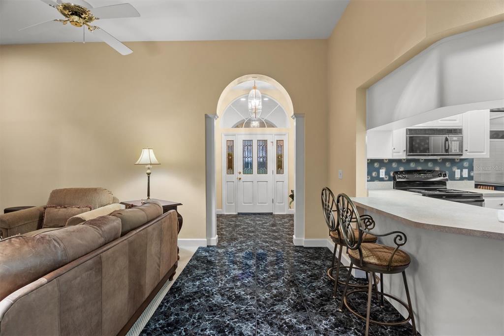 A living room and kitchen area with dark marble-look tile flooring and a front entryway — 1142 LONGWOOD OAKS BOULEVARD, LAKELAND, FL