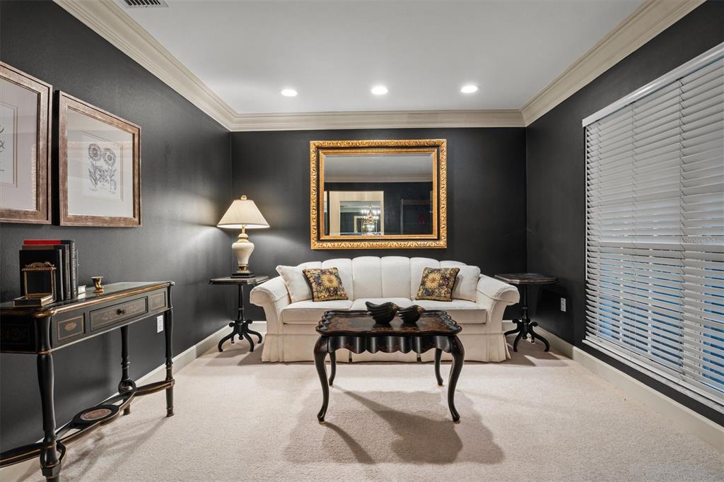 A formal living room features dark walls, a white sofa, a gold mirror, and carpeted floors — 1142 LONGWOOD OAKS BOULEVARD, LAKELAND, FL