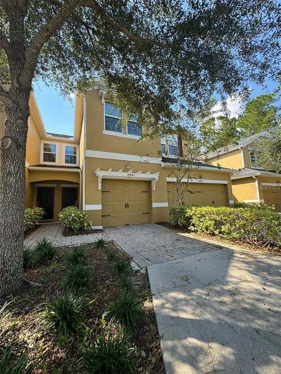 A two-story tan house features a two-car garage, a paved driveway, and mature landscaping — 14442 DESERT HAVEN STREET UNIT 4305, WINDERMERE, FL