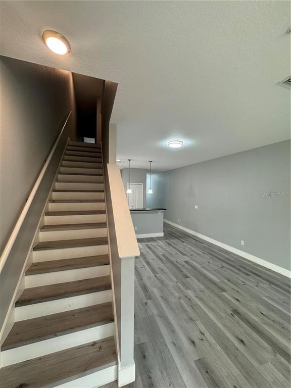 A staircase with wood-look treads leads upward next to an open living area with gray flooring — 14442 DESERT HAVEN STREET UNIT 4305, WINDERMERE, FL