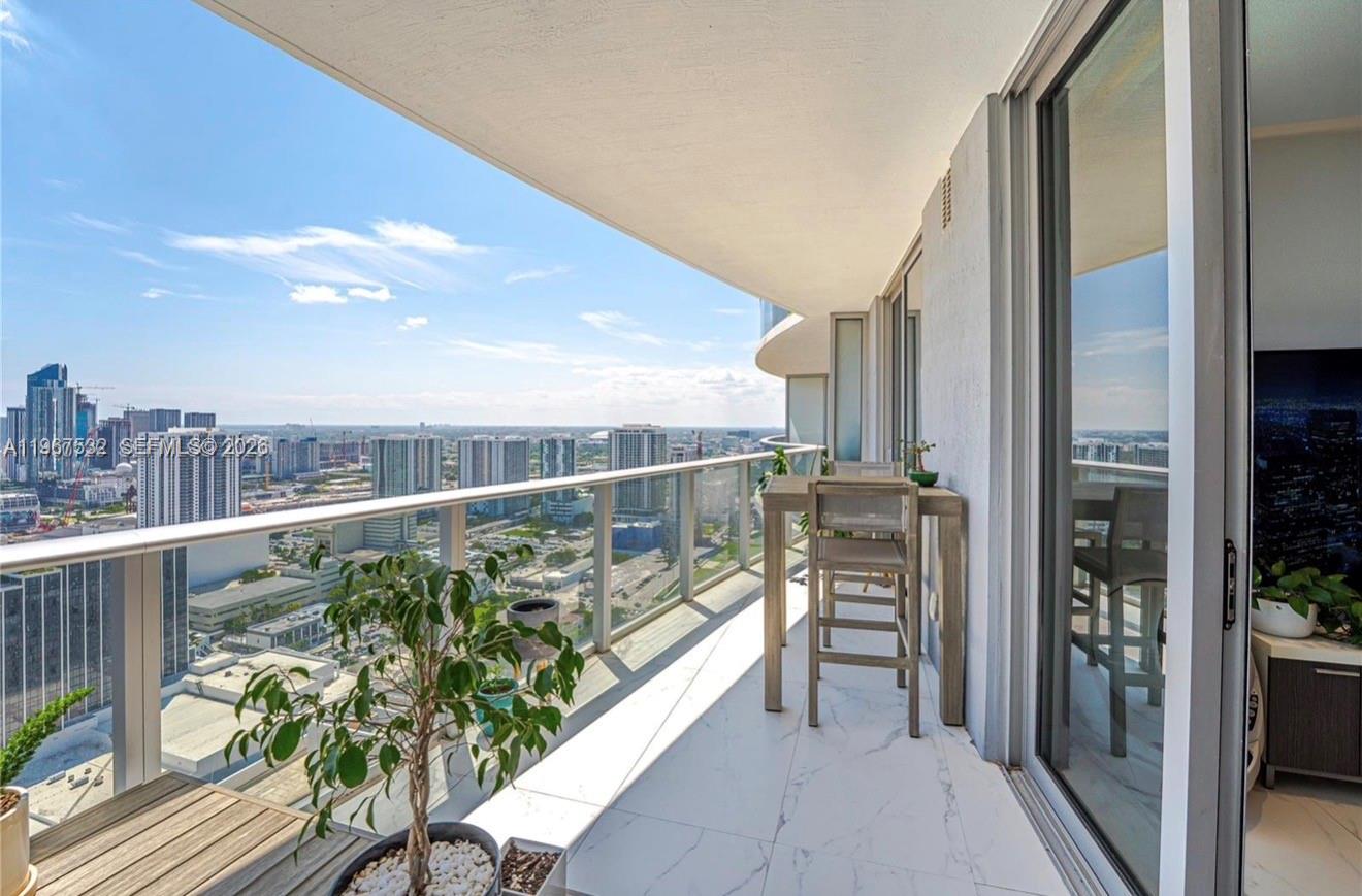A high-rise balcony features white marble-look tile flooring, a small dining set, and city views — 488 NE 18th St # 4304, Miami FL 33132, MIAMI, FL