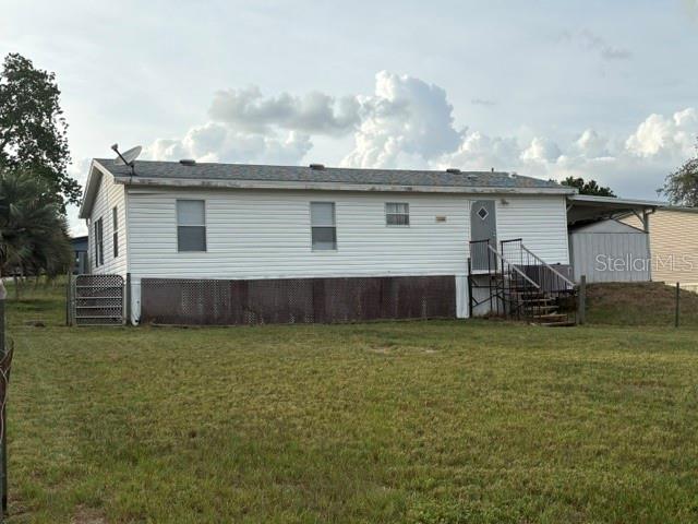 A white manufactured home with a metal skirt and a side carport sits on grass — 13225 PLUM LAKE CIRCLE, MINNEOLA, FL