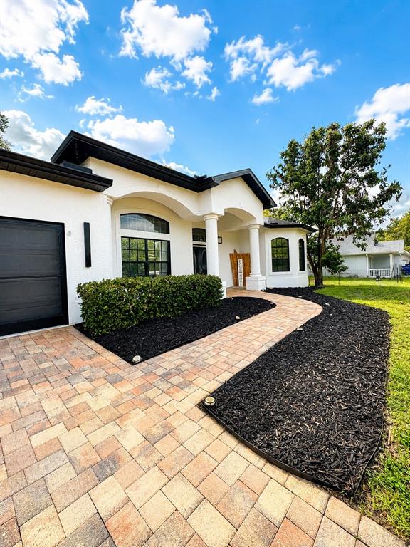 A white house exterior features a paver walkway, black mulch, and a dark garage door — 12716 BALSAM AVENUE, HUDSON, FL