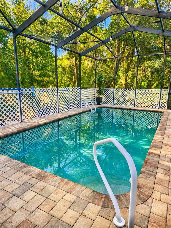 A rectangular swimming pool with a brick paver deck is enclosed by a screened lanai — 12716 BALSAM AVENUE, HUDSON, FL