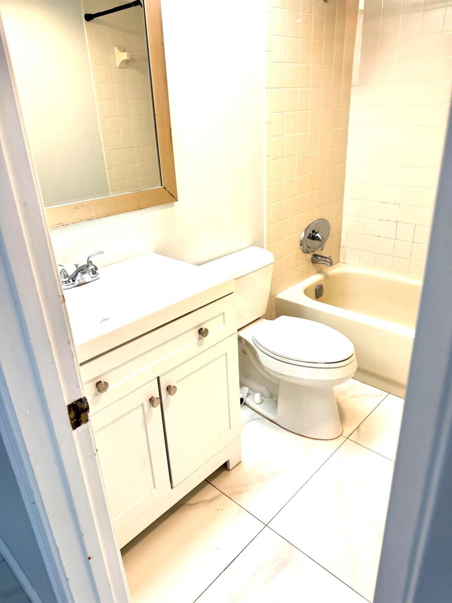 A bathroom features a white vanity, a toilet, and a bathtub with beige tiled walls — 4121 Oak Terrace Drive, FL 33463, FL