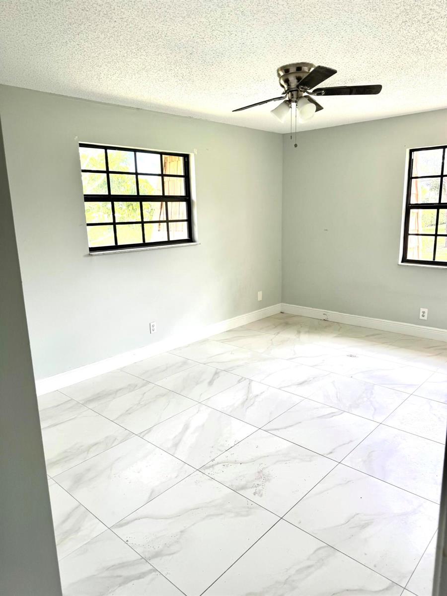 An empty room features light gray walls, white marble-look tile flooring, and a ceiling fan — 4121 Oak Terrace Drive, FL 33463, FL