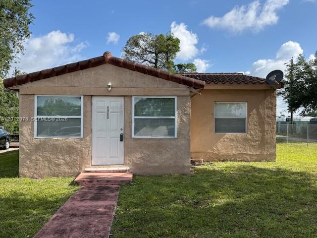 A single-story tan stucco house features a brown tiled roof and a white front door — 6013 SW 34th St, Miramar FL 33023, MIRAMAR, FL