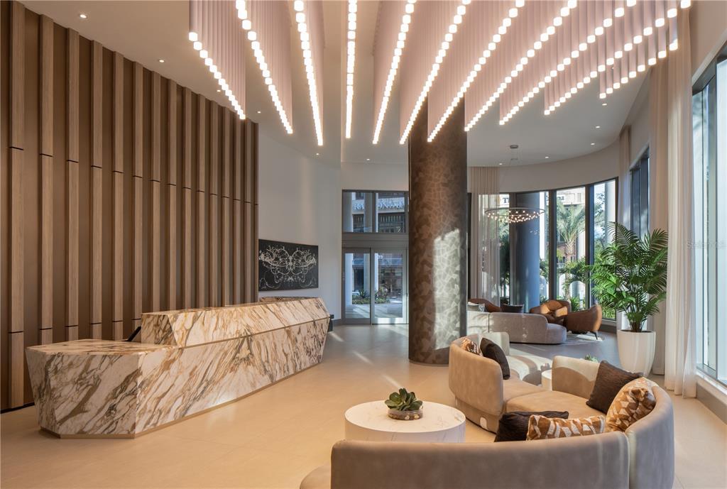 A modern lobby features a marble reception desk, vertical wood paneling, and hanging pendant lights — 275 1ST AVENUE S UNIT 1502, ST PETERSBURG, FL