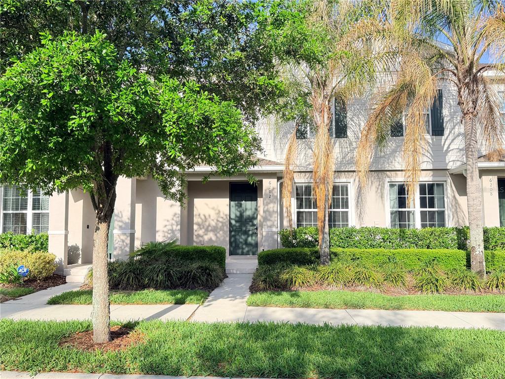 A two-story townhouse exterior features a dark front door, palm trees, and manicured hedges — 6212 ARALIA IVY LANE, WINTER GARDEN, FL
