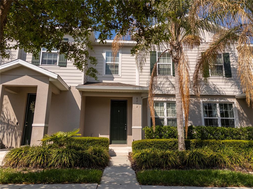 A two-story townhouse exterior features light siding, dark shutters, a front porch, and landscaping — 6212 ARALIA IVY LANE, WINTER GARDEN, FL