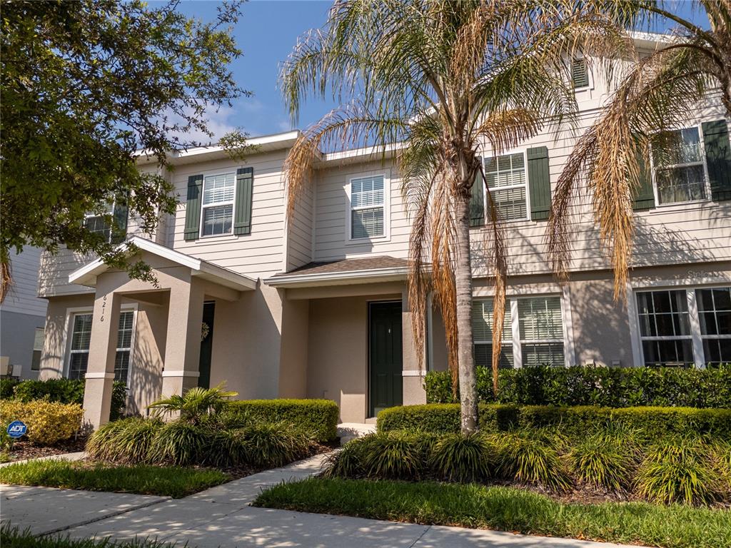 A two-story townhouse exterior features beige siding, green shutters, and a palm tree in front — 6212 ARALIA IVY LANE, WINTER GARDEN, FL