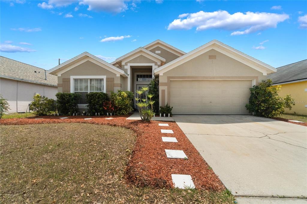 A single-story suburban house with a tan stucco exterior, a two-car garage, and landscaping — 640 LADY DIANA DRIVE, DAVENPORT, FL
